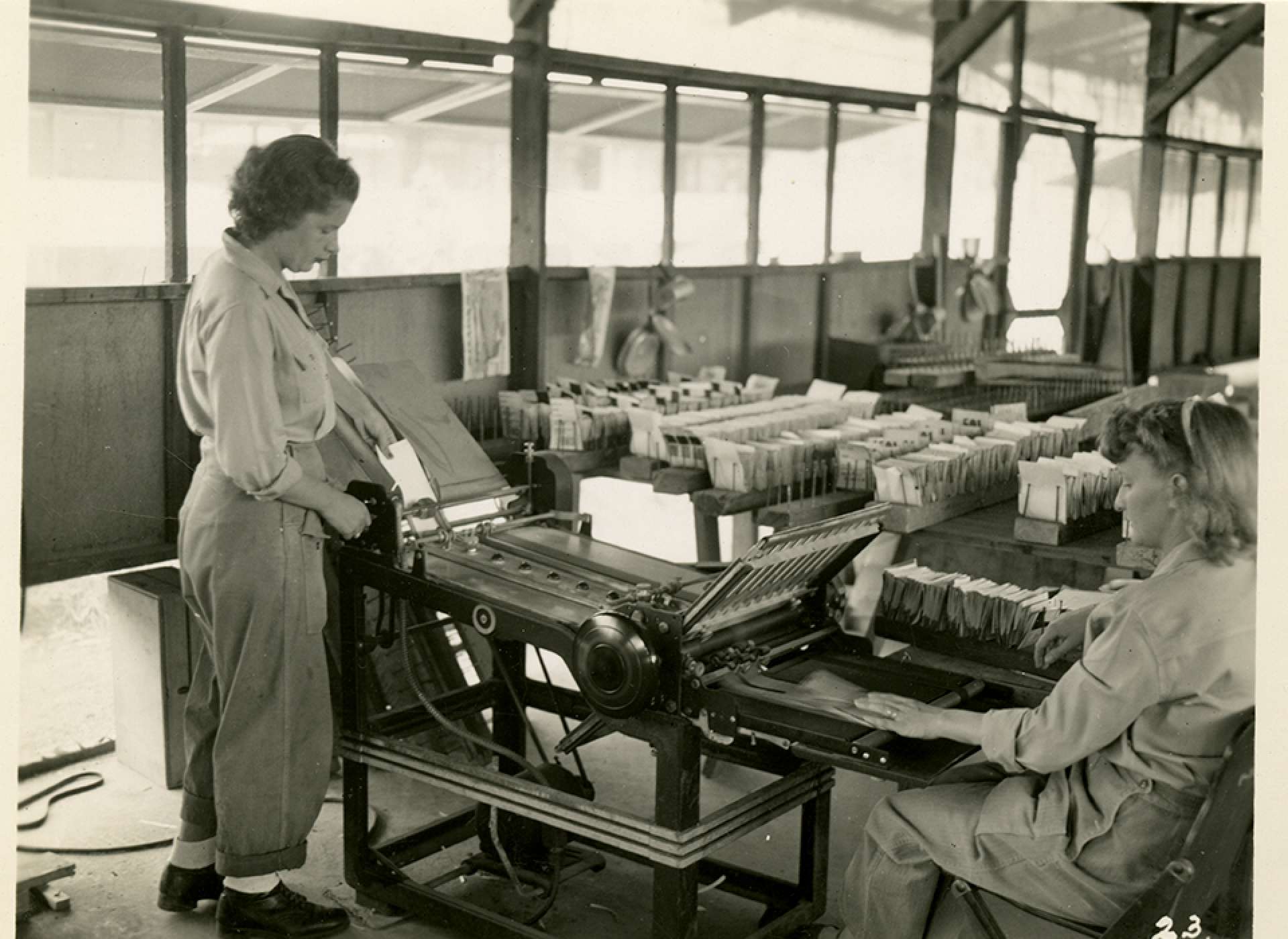 V-mail operation in the field at APO 929. “On this machine the letters are folded to correct size for insertion into V-Mail envelops, an operation which requires about eight minutes per roll. In the background are racks of folded letters.&quot;