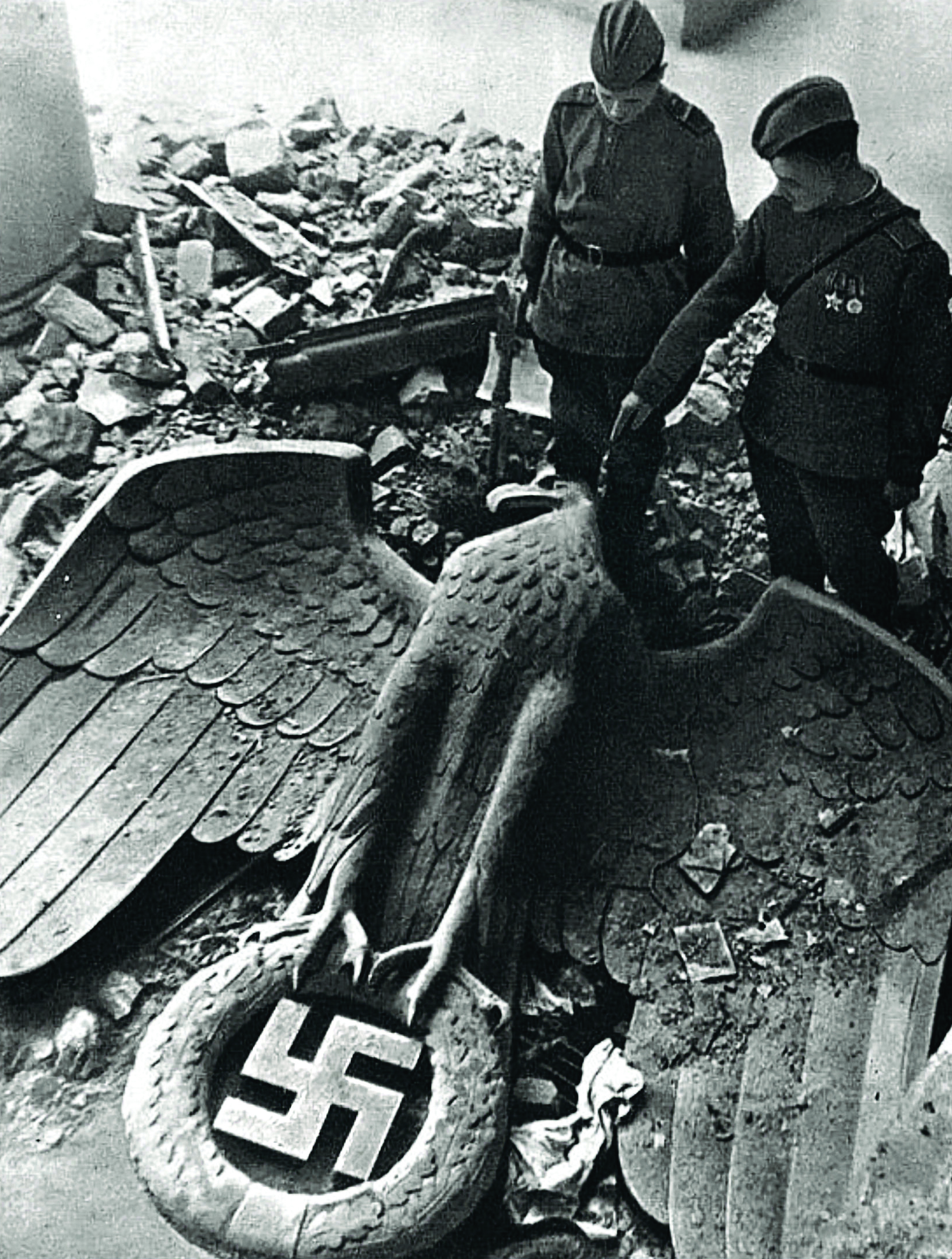 Two soldiers look at the ruins of Nazi statues and symbols during WWII.