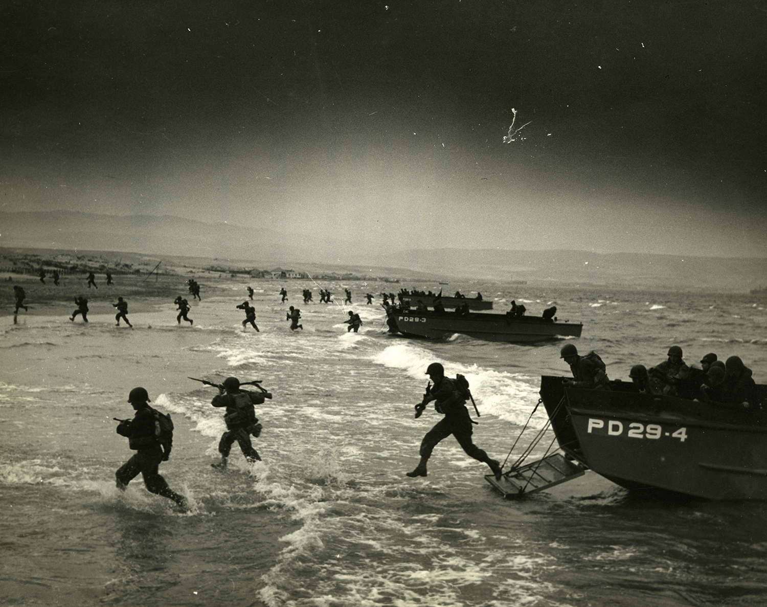 Soldiers run onshore from a boat during WWII