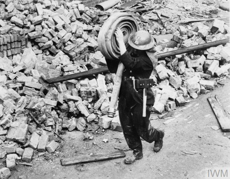 Fireman carries rolled hose to hose dump after a night&#039;s work, passing bricks and other rubble.