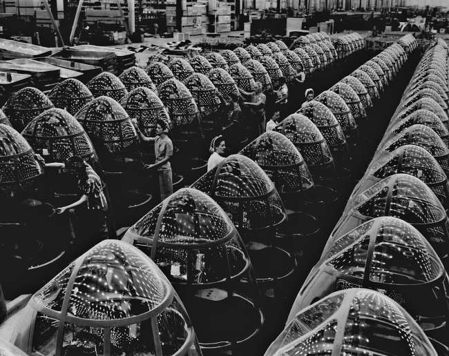 Factory with rows of airplane noses being inspected by women during WWII