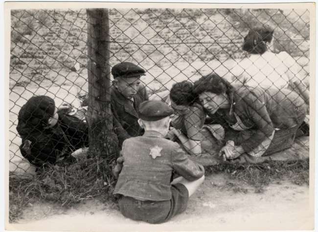 A child who has been selected for deportation, bids farewell to his family through the wire fence of the central prison, during the &quot;Gehsperre&quot; action in the Lodz ghetto