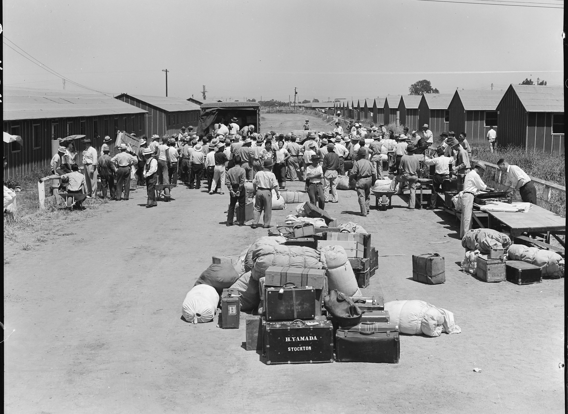 Japanese-Americans are moved into buildings as their belongings lie scattered on the pavement behind them.
