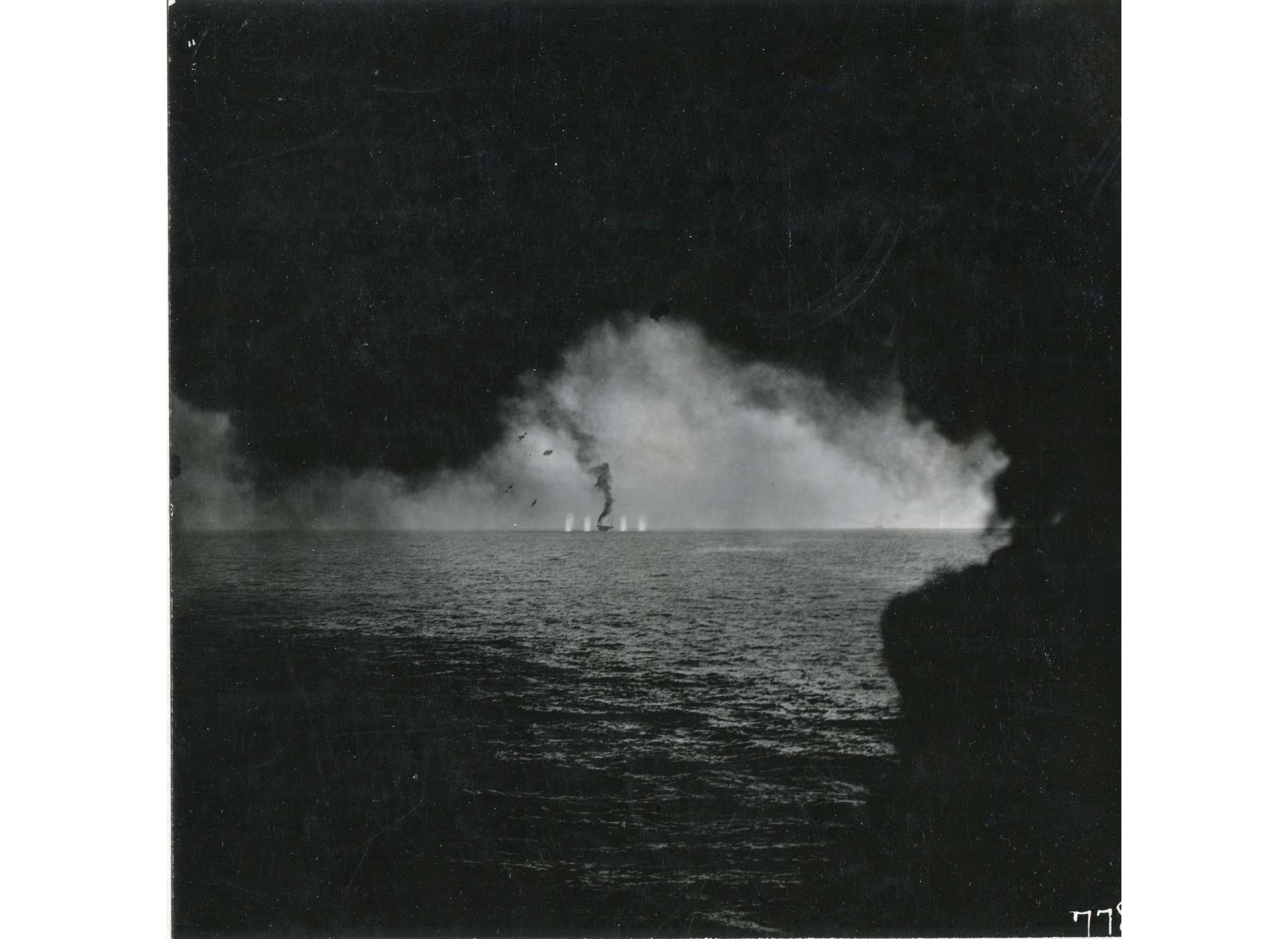 Funnel smoke from USS Kitkun Bay (CVE-71) frames straddle shot on USS Gambier Bay (CVE-73). Note Japanese cruiser on the horizon.