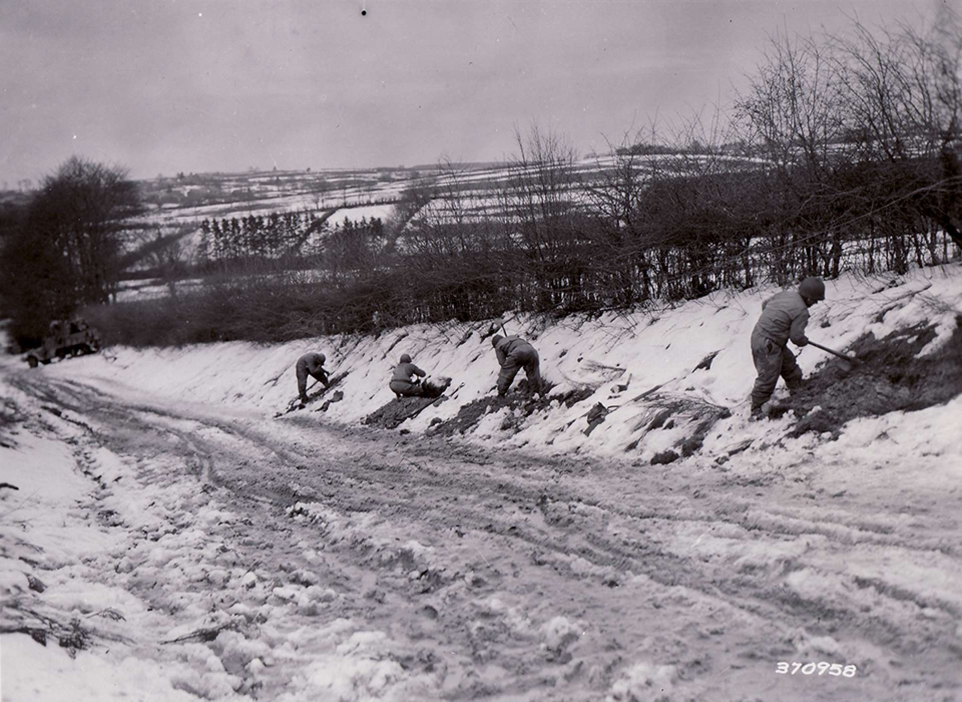 2nd Infantry Division soldiers dig in on a road bank and prepare defensive positions on the end of the Elsenborn Ridge on December 20, 1944. The National WWII Museum Digital Collections.