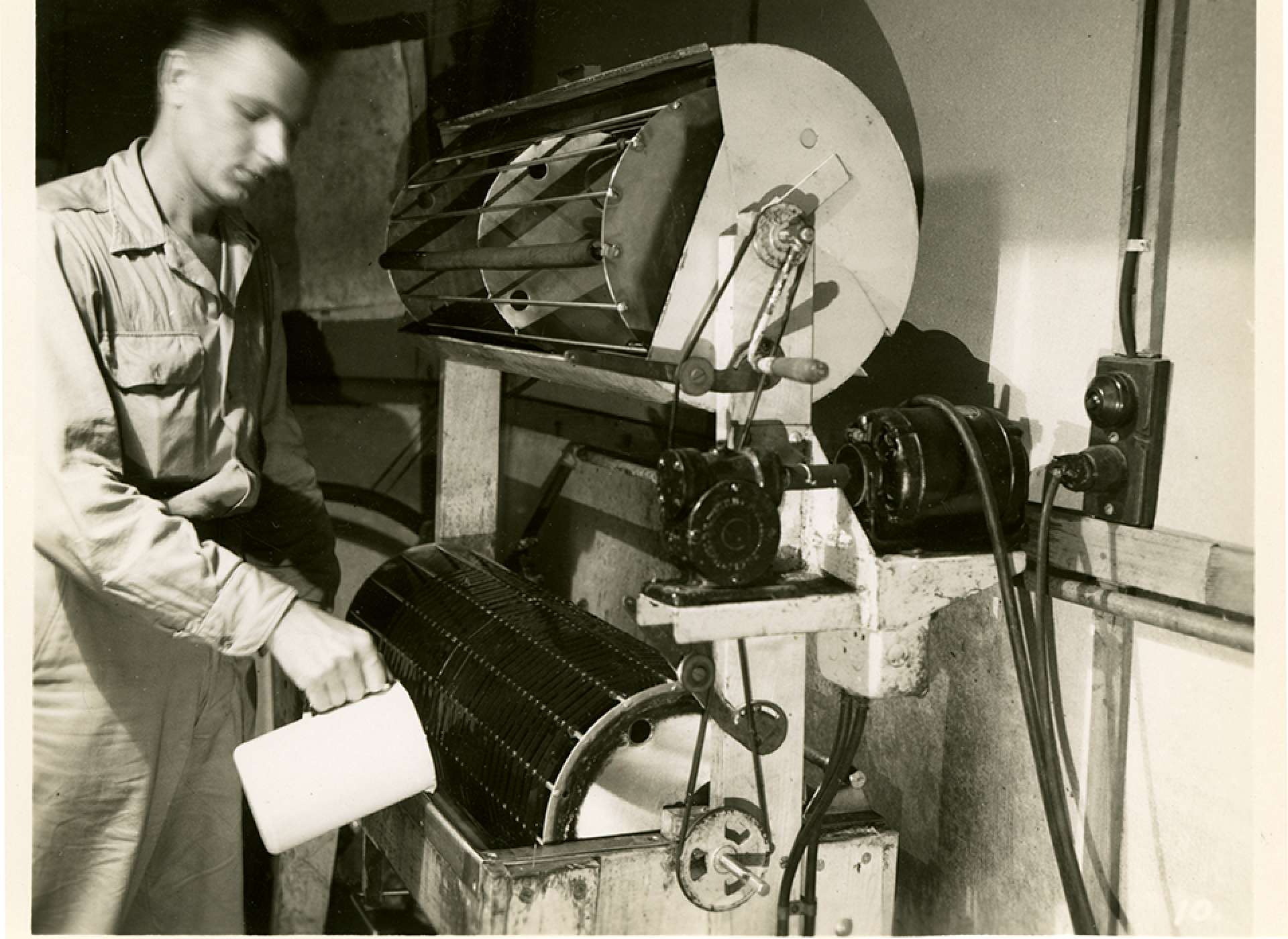 V-mail operation in the field at APO 929.”The next step is the processing of the film, which is done both on automatic machines which do individual rolls. In this shot the operator has completed the developing and is pouring in the hypo or fixing bath, after which the film will be subjected to a water spray to wash it thoroughly. It is then fed on to the upper reel which it is thoroughly dried by means of a warm air stream.”
