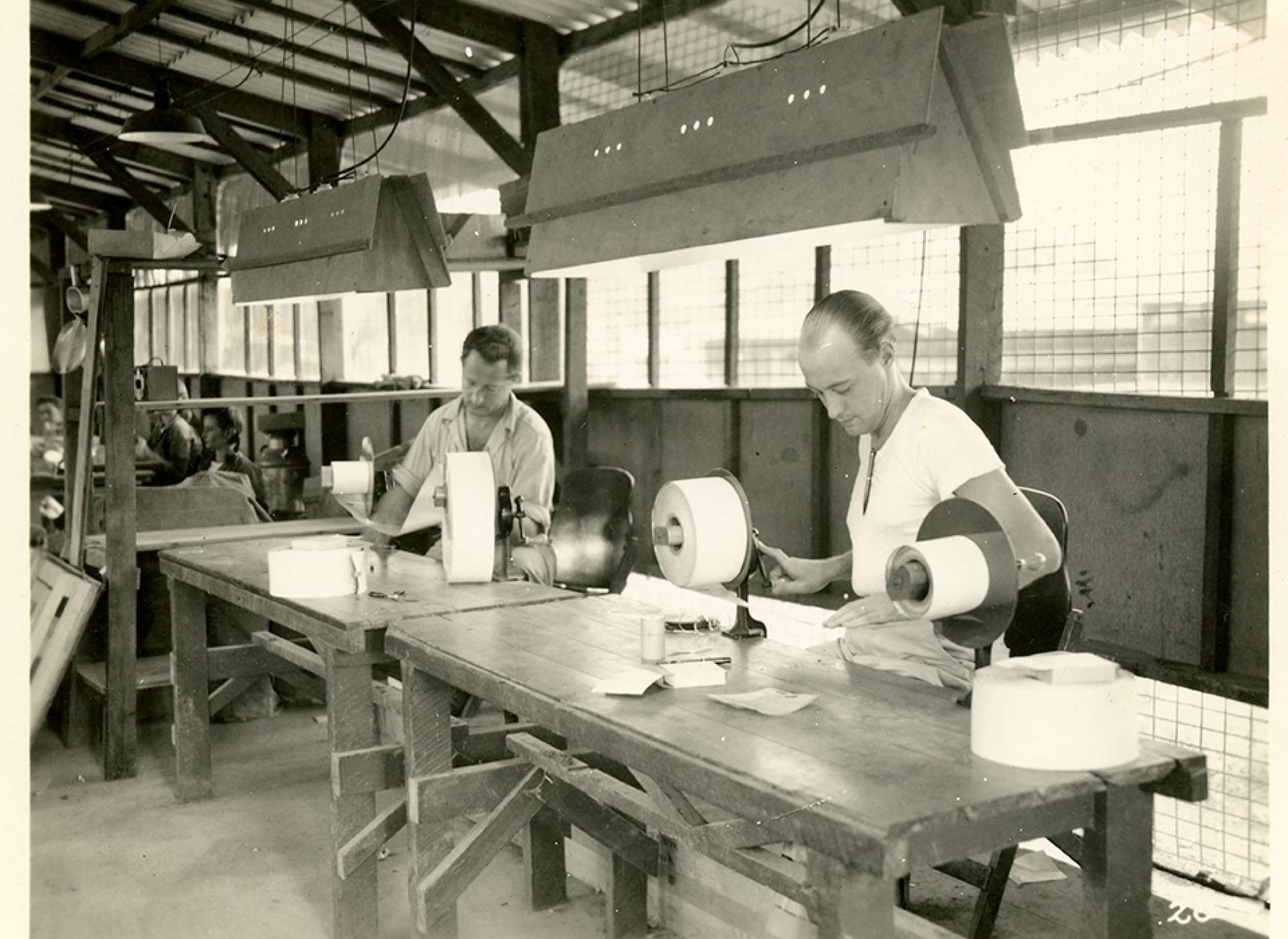V-mail operation in the field at APO 929. “Paper inspection. At these tables each roll of finished work is inspected letter by letter and all badly reproduced letters are marked out. Where possible, an attempt is made to produce a better print in the Reprint department. Letters which cannot be satisfactorily reproduced are either sent back to the States to be rephotographed or to be sent via regular mail.” Port Moresby, Papua New Guinea. 1944