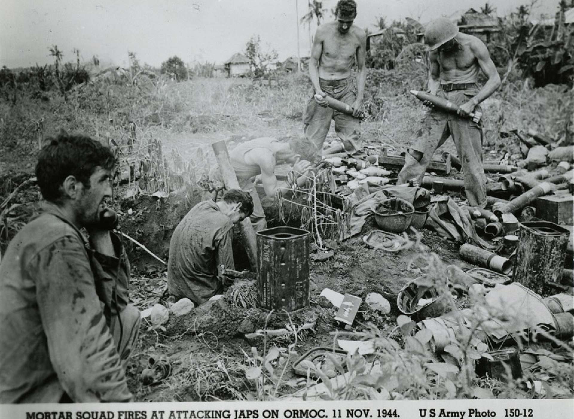 Two United States Army soldiers holding mortar bombs next to two other soldiers who are firing the mortar; another soldier is talking into a field telephone. Official caption on front: &quot;Mortar squad fires at attacking Japs on Ormoc, 11 Nov. 1944. US Army Photo 150-12.&quot; Ormoc, Leyte, Philippines. 11 November 1944. Gift in memory of Sgt. Lyle E. Eberspecher, 2013.495.930