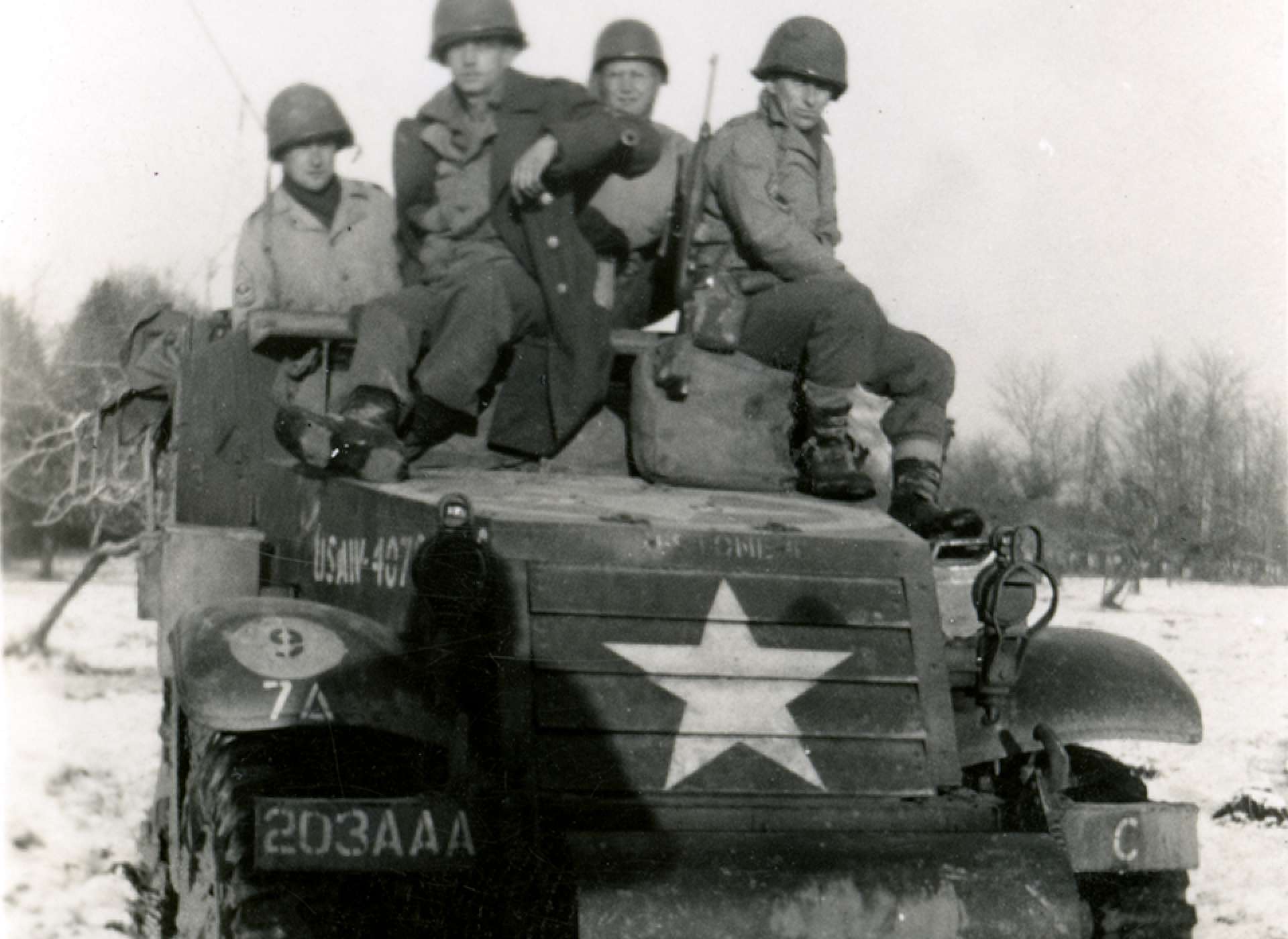Four American soldiers riding on a half-track during the Battle of the Bulge