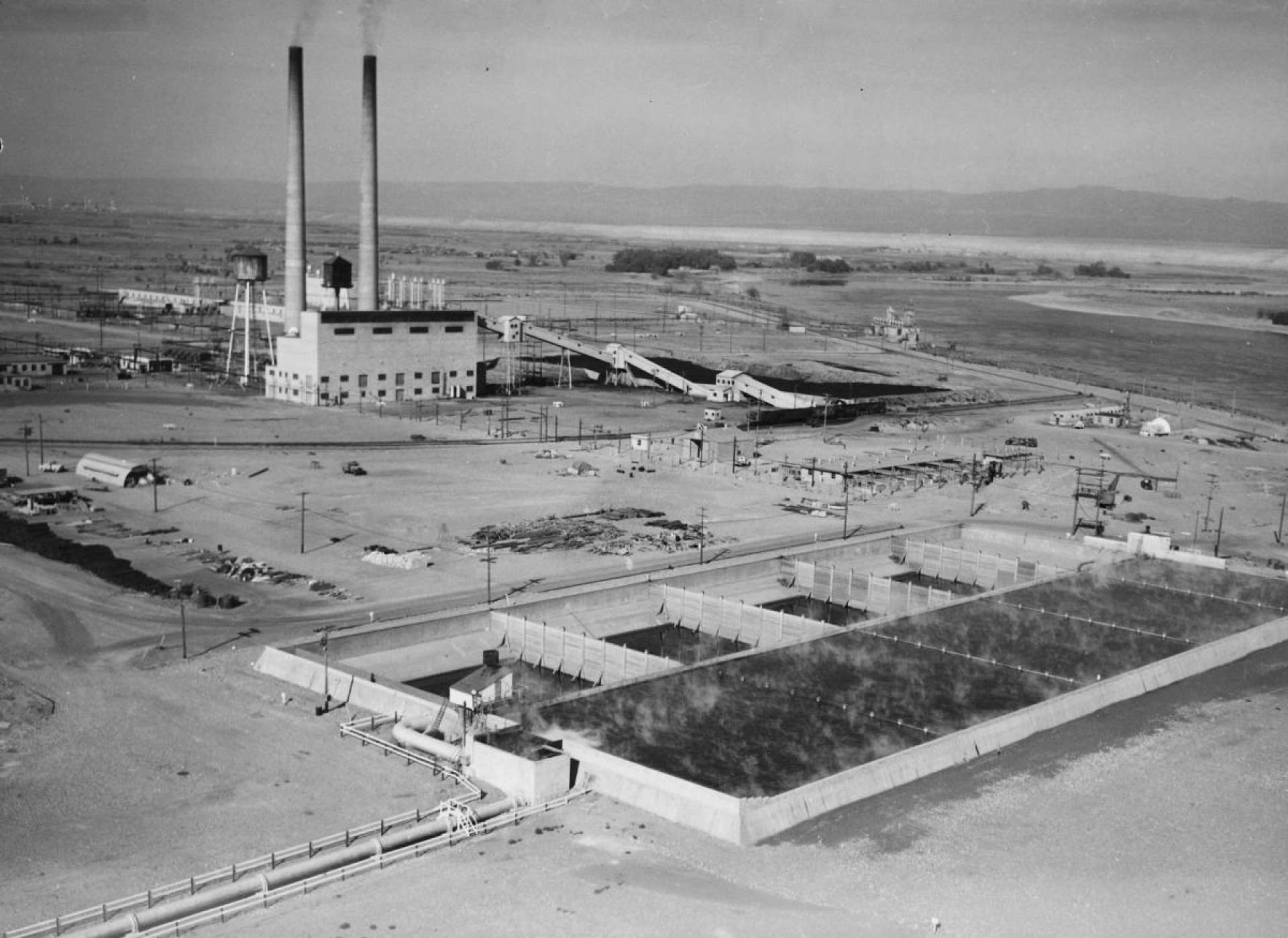 An aerial view (ca 1945) of the Hanford site, over the retention basins where water was cooled after it had flowed over the reactor (building in the background). After the water cooled to ambient temperature it was returned to the Columbia River, which can be seen in the upper right of the image. (from the archives of the Department of Energy)