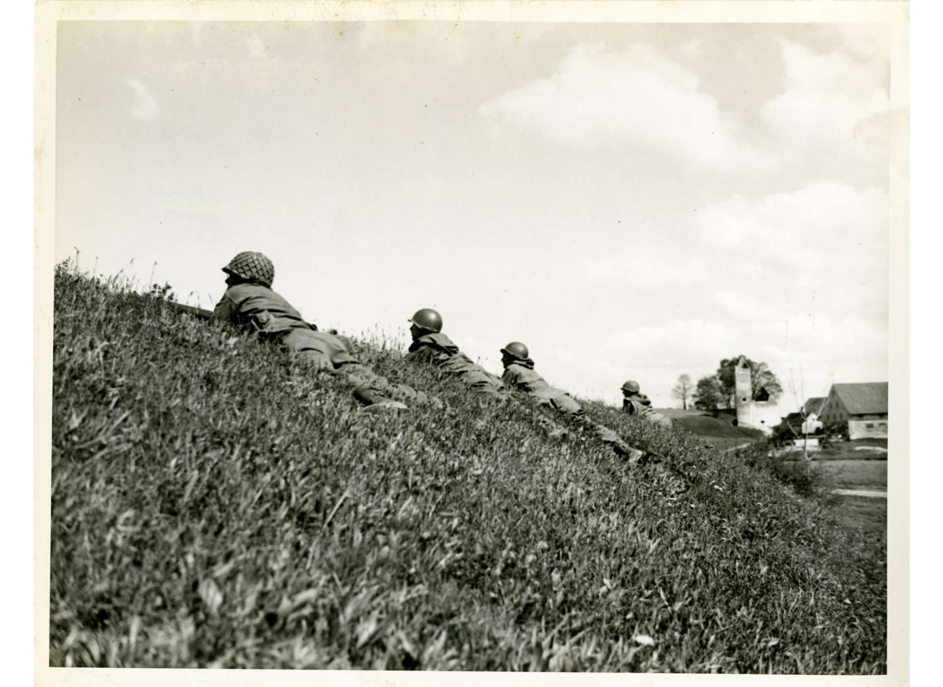 Soldiers from the US 42nd Infantry Division take cover on a ridge in a field near Dachau, April 29, 1945. They were under fire from a group of 30 SS troops. US Army Signal Corps Photo, Gift in Memory of Allan Voluck, from the Collection of The National World War II Museum, 2015.111.084.