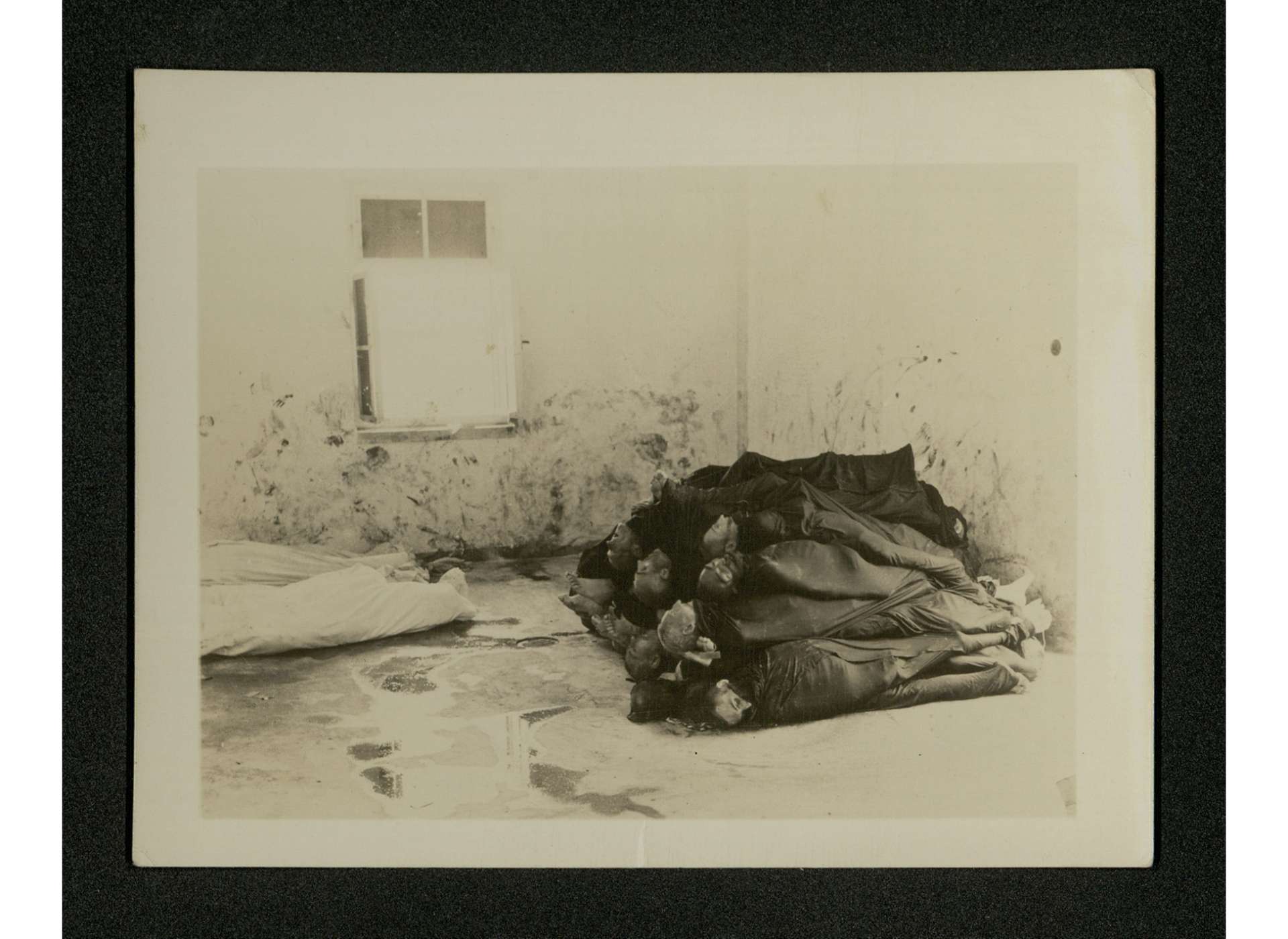 Corpses wrapped and piled in a cement room where blood smears are to be seen on the walls. US Army Signal Corps photo, Gift of the Acosta Family, from the Collection of The National World War II Museum, 2014.057.028.