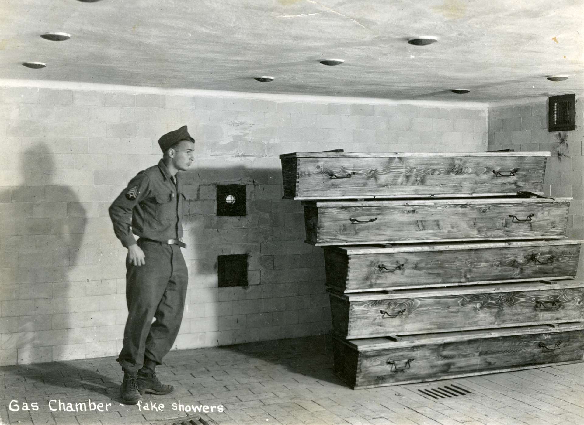 US soldier standing in the gas chamber in the Dachau concentration camp, 1945. Five wooden caskets are stacked along the wall. US Army Signal Corps photo, Gift of the United States Holocaust Memorial Museum, from the Collection of The National World War II Museum, 2009.373.061.
