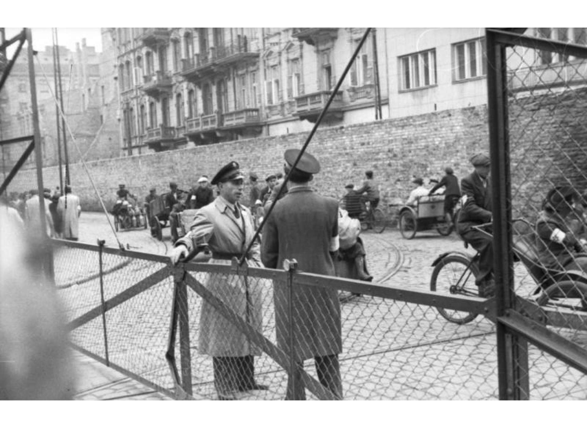 Men of the Jewish Order Service at the gates of the Warsaw Ghetto, June 1942. Credit: Bundesarchiv Bild 101I-270-0298-11, Polen, Ghetto Warschau, Drahtzaun.