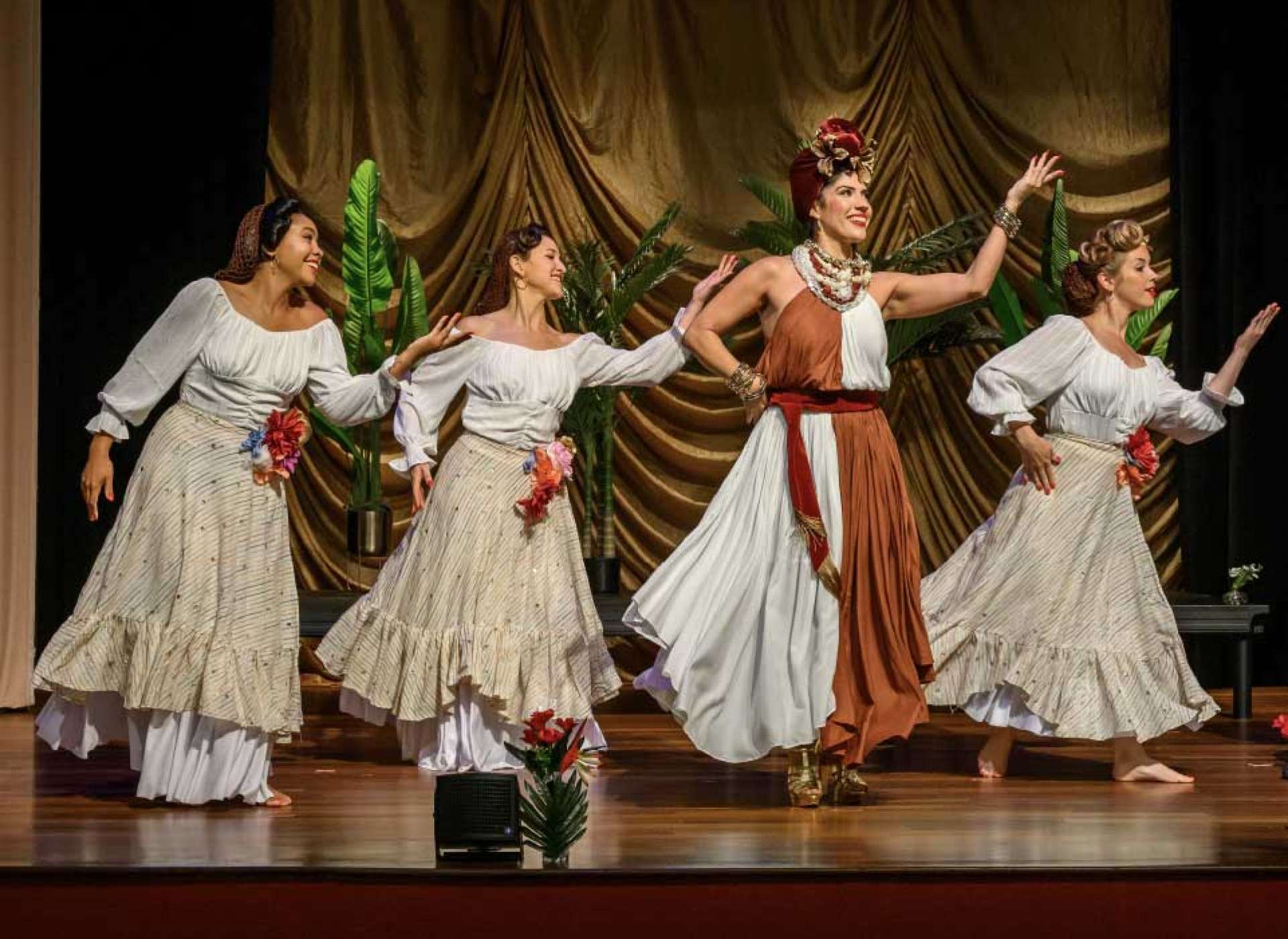 Performers in traditional Latin costumes dance on stage at BB's Stage Door Canteen, accompanied by a live band playing guitar, trombone, bass, and saxophone, with Carmen Miranda show posters displayed in front of the musicians.