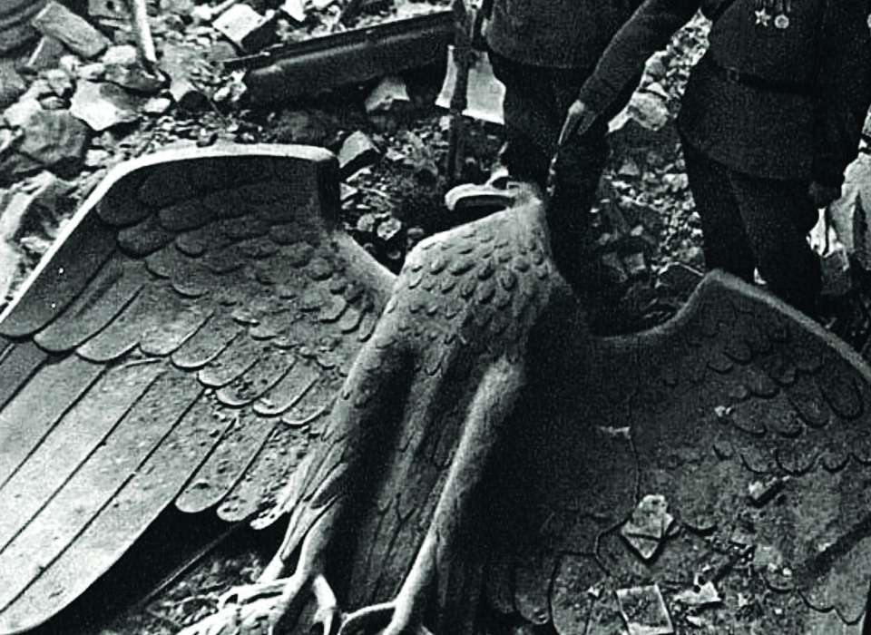 Two soldiers look at the ruins of Nazi statues and symbols during WWII.