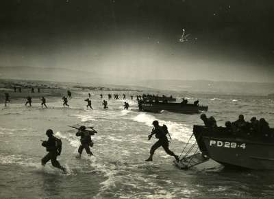 Soldiers run onshore from a boat during WWII